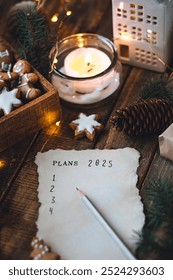 Rédiger à la main les résolutions du Nouvel An 2025 en décembre, le soir du Nouvel An. Plan, objectifs, idées, projets. Ambiance de vacances à la maison, lumières de Noël, décoration festive, biscuits au pain d'épices faits maison