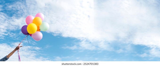 Banner Cheerful cute girl holding balloons running green meadow white cloud and blue sky with happiness. Panorama Hands holding vibrant air balloons happy times summer sunlight outdoor copy space