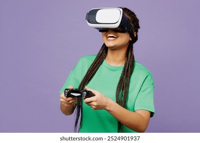 Jovem mulher com dreadlocks usa camiseta verde roupas casuais segura na mão joga jogo de pc com joystick console assistindo em fone de ouvido vr gadget de pc isolado em fundo roxo simples. Conceito de estilo de vida