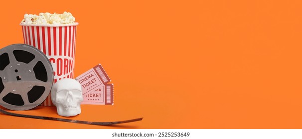 Kekili filem, tiket pawagam, popcorn dan tengkorak pada latar belakang oren dengan ruang untuk teks. Filem Halloween