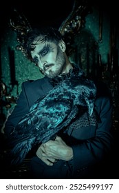 Un bărbat brunet elegant, într-un costum negru, cu jabot și machiaj artistic negru, stă cu tristețe într-o cameră întunecată de epocă, cu un corb. Domnul Întunecat. Halloween. Fantezie.