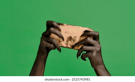 Creepy halloween devil monster hand black paint with black nails plays video game on smartphone, isolated on chroma key green screen background, workspace mockup.
