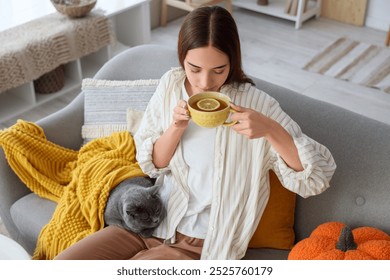 Wanita muda dengan kucing Inggris yang lucu minum teh hijau di rumah pada hari musim gugur