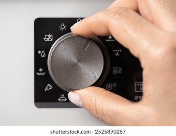 Fra ajustéiert modernen wäissen Uewen an der Kichen. Weiblech Hand dréckt a dréit Knäppercher op Uewen Kontrollpanel. Closeup