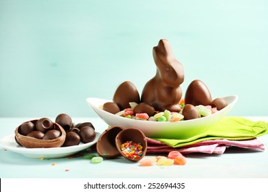 Schokoladen-Ostereier und Kaninchen auf Platte, auf farbigem Holzhintergrund