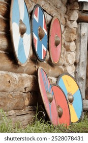 Escudos vikings coloridos encostados em uma parede rústica de madeira, exibindo desenhos intrincados e artesanato histórico. Representação perfeita da cultura e arte viking.