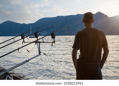 Aventures de pêche, pêche à la carpe. Homme pêchant sur un grand lac au coucher du soleil. Pêcheur debout et de dos, à côté de matériel de pêche, lac Majeur, Italie