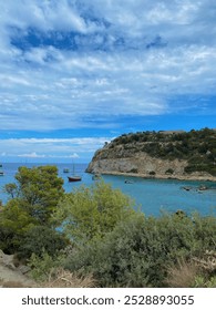 Yunanistan, Rodos'taki Anthony Quinn Koyu'nun güzel yaz manzarası. Turkuaz sular, kayalık uçurumlar ve yemyeşil bitki örtüsü, kısmen bulutlu bir gökyüzünün altında çarpıcı bir Akdeniz manzarası yaratıyor.