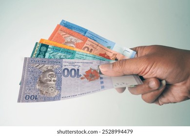 RM 100、50、20、10、5 を含むさまざまな額面のマレーシア リンギット紙幣を持っている手のクローズ アップ。白い背景に分離されています。