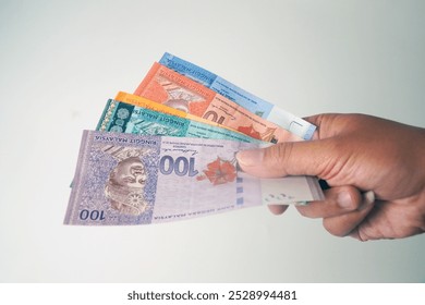 RM 100、50、20、10、5 を含むさまざまな額面のマレーシア リンギット紙幣を持っている手のクローズ アップ。白い背景に分離されています。