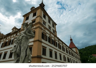 Außenansicht von Schloss Eggenberg in Graz, Steiermark, Österreich, Europa. Barocker Schlosskomplex ist UNESCO-Weltkulturerbe. Statue des Kriegsgottes Mars im Vordergrund. Verzierter Turm mit Säulenfassade
