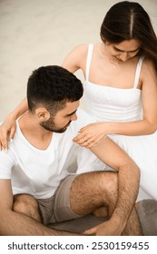 Pamje nga afër e sipërme e çiftit të ri të ulur në rërë, një vajzë që vendos duart mbi supet e djalit