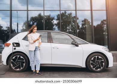 O tânără stă lângă mașina ei electrică și își folosește smartphone-ul în timp ce se încarcă. Scena întruchipează tehnologia ecologică și un stil de viață modern, conectat într-un cadru urban.