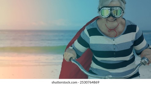 海滩上，穿着超级英雄服装骑自行车的白人老年妇女身上的光斑。踏板日意识概念