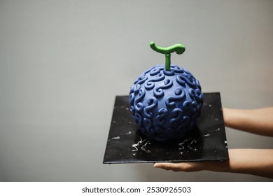 تحمل يد شخص كعكة عيد ميلاد أرجوانية تشبه "Gomu Gomu No Mi" في سلسلة الأنمي One Piece. ضوء طبيعي وخلفية بيضاء.