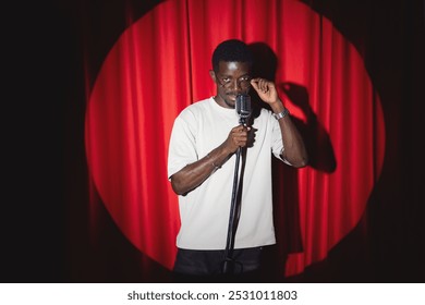 Professional energetic african american man jazz or pop music singer is performing song with retro microphone on stage with red curtains.
