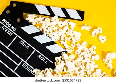 Zbliżenie czarno-białego drewnianego klapsa filmowego z popcornem na żółtym tle, koncepcja rozrywki kinowej
