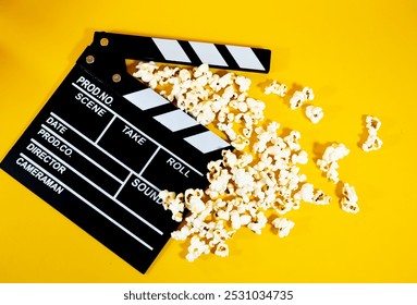 Widok z góry na czarno-biały drewniany klaps filmowy z popcornem na żółtym tle, koncepcja produkcji filmowej i rozrywki