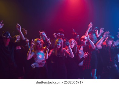 Amigos fantasiados, meninos e meninas, participando da festa de Halloween, comemorando com bebidas não alcoólicas e guloseimas, dançando e rindo. Evento de boate. Conceito de Halloween, feriado, festa, lazer
