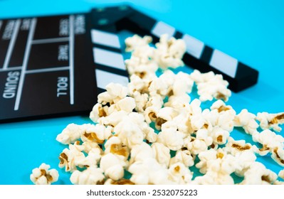 Zbliżenie czarno-białego drewnianego klapsa filmowego z popcornem na niebieskim tle. Obraz poziomy, koncepcja kina i zabawy