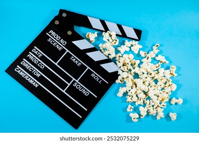 Widok z góry na czarno-biały drewniany klaps filmowy z popcornem na niebieskim tle, koncepcja produkcji filmowej i rozrywki