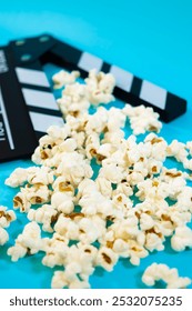 Pionowy obraz czarno-białego drewnianego klapsa filmowego z popcornem na niebieskim tle, koncepcja kina i zabawy