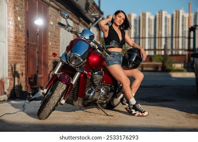 Brunetka v šortkách pózuje na červenej motorke.