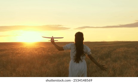 Airplane in hand of girl child playing in sunny wheat field. Aviator child girl, dreams and fantasies about flight. Happy childhood. Teenager dreams of flying on airplanes and traveling world. Sun sky