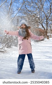 Winter lifestyle portret van vrolijk meisje in gebreide muts die sneeuw in de lucht gooit. Kind lacht en heeft plezier in het sneeuwpark. Sneeuwvlokken vallen naar beneden. Vrijheid en geluk concept.