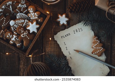 Rédiger à la main les résolutions du Nouvel An 2025 en décembre, le soir du Nouvel An. Plan, objectifs, idées, projets. Ambiance de vacances à la maison, lumières de Noël, décoration festive, biscuits au pain d'épices faits maison