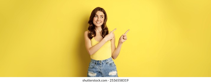 Chân dung cô gái mùa hè sành điệu, người phụ nữ tóc nâu chỉ đường, chỉ tay sang trái, quảng cáo, đứng trên nền vàng. Sao chép không gian