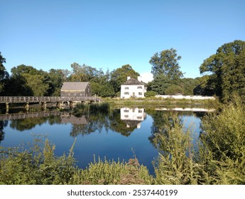 Una casa storica a Sleepy Hollow riflessa sulle acque calme lì vicino. Questa fotografia mette in risalto la tranquillità della zona, circondata da una vegetazione lussureggiante, creando una vista pittoresca.