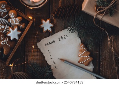 Rédiger à la main les résolutions du Nouvel An 2025 en décembre, le soir du Nouvel An. Plan, objectifs, idées, projets. Ambiance de vacances à la maison, lumières de Noël, décoration festive, biscuits au pain d'épices faits maison