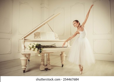 El piano blanco se encuentra en un interior grande y luminoso, una chica parada frente a él, ella está bailando. en las teclas del piano hay rosas blancas.