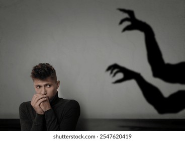 Un joven se asusta al ver las manos de un monstruo que intenta alcanzarlo. Sombra espeluznante en una pared gris