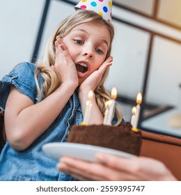Gros plan sur une petite fille souriante et excitée par son gâteau d'anniversaire. La famille, coiffée de chapeaux de fête, célèbre l'anniversaire de leur fille à la maison. La petite fille souffle les bougies de son gâteau d'anniversaire.
