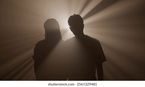 Силуэты мужчины и женщины, обнимающихся и идущих к камере на фоне яркого теплого цветного прожектора, изолированные на студийном фоне крупным планом.