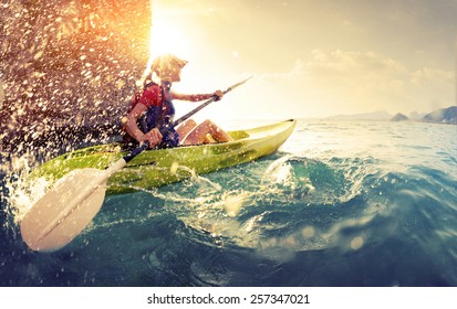 Señorita remando duro el kayak con muchas salpicaduras cerca del acantilado en un día soleado