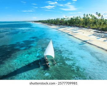 青い海に浮かぶヨット、日の出に照らされた白い砂浜の空撮。ザンジバルでの夏休み。ボート、澄んだ水、緑のヤシの木、空のあるトロピカルな風景。ドローン空撮。エキゾチックな風景。