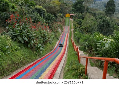 Junger Mann reitet auf einer bunten Regenbogen-Plastikrutsche im Extrem-Abenteuerpark im Bergregenwald in El Salvador.