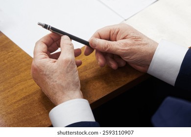 Mani rugose di un uomo anziano che tiene una penna. Un autorevole politico o uomo d'affari siede a un tavolo con fogli bianchi e documenti. Foto. Nessun volto. Messa a fuoco selettiva. Primo piano.