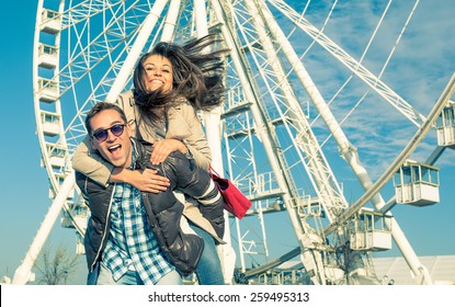 Mann gibt Huckepack - trägt seine Freundin nach einem Einkaufstag in der Stadt auf dem Rücken. Bild eines jungen fröhlichen Paares vor dem Riesenrad