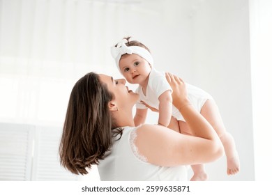 A mother with a small child or infant is playing at home by the window in the children's room. Happy maternity leave, mom's love and care, space for text.