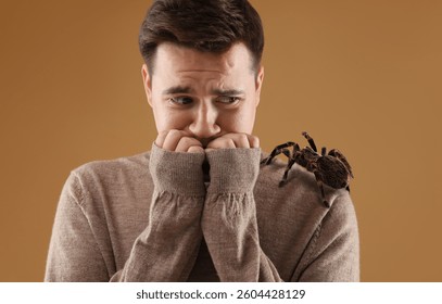 一个惊恐的男人肩上趴着一只蜘蛛，背景是浅棕色。蜘蛛恐惧症概念