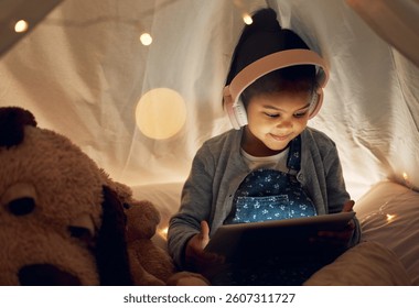 Kız, çocuk ve gece çadırda tabletle rahatlayıp çizgi film ve video izlemek için kulaklık takıyorlar. Kız çocuk, evde internetin eğlence, çevrimiçi oyunlar ve eğitim için olmasıyla mutlu ve rahat.