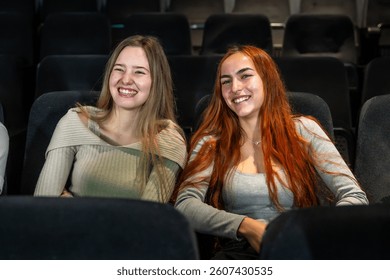 Dvije sretne mlade žene sjede u udobnim kino sjedalima, uživaju u filmu i smiješe se