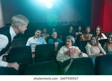 Ljudi gledaju film i jedu kokice u kinu, komunicirajući s razvodnikom