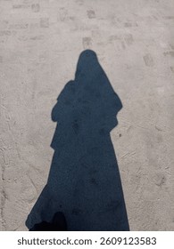 Schattensilhouette einer Frau mit Hijab auf sandigem Boden im Sonnenlicht. Minimalistisch und geheimnisvoll. Perfekt für Themen wie Identität, Einsamkeit und Reflexion.