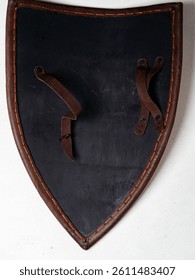 Detalhe de um escudo medieval de couro com bordas reforçadas, alças para os braços e materiais rústicos que lhe conferem um aspecto único.