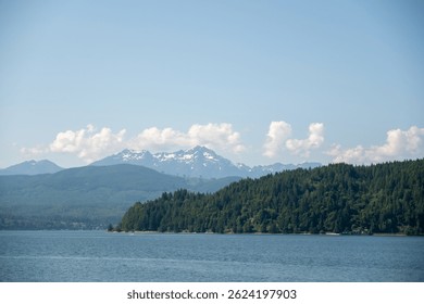 Puget Sound tiho teče pod mehkim modrim nebom, z oddaljenim pogledom na olimpijsko gorovje, ki kuka nad gozdno mejo, posneto 31. maja 2019 v Seattlu, WA, ZDA.